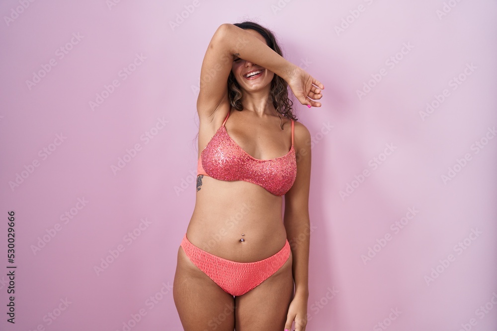 Naklejka premium Young hispanic woman wearing lingerie over pink background covering eyes with arm smiling cheerful and funny. blind concept.