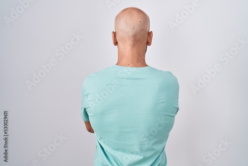 Middle age bald man standing over white background standing backwards looking away with crossed arms photo