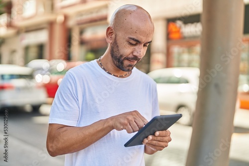Young bald man using touchpad with serious expression at street