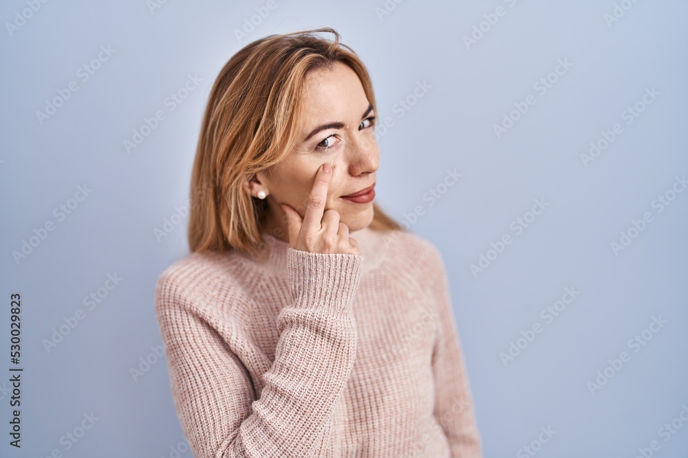 Hispanic woman standing over blue background pointing to the eye watching you gesture, suspicious expression Hispanic woman standing over blue background pointing to the eye watching you gesture, suspicious expression