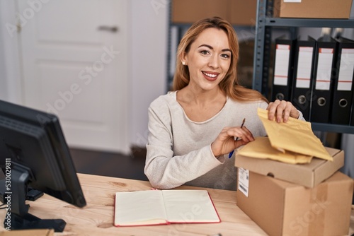 Young woman ecommerce busines worker writing on notebook holding package at office