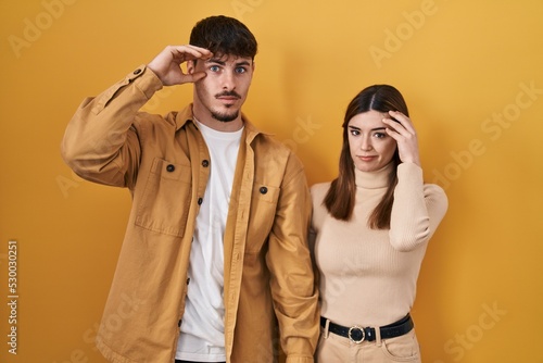 Young hispanic couple standing over yellow background worried and stressed about a problem with hand on forehead, nervous and anxious for crisis