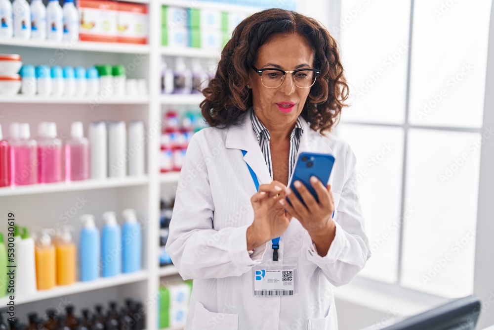 Middle age woman pharmacist using smartphone working at pharmacy