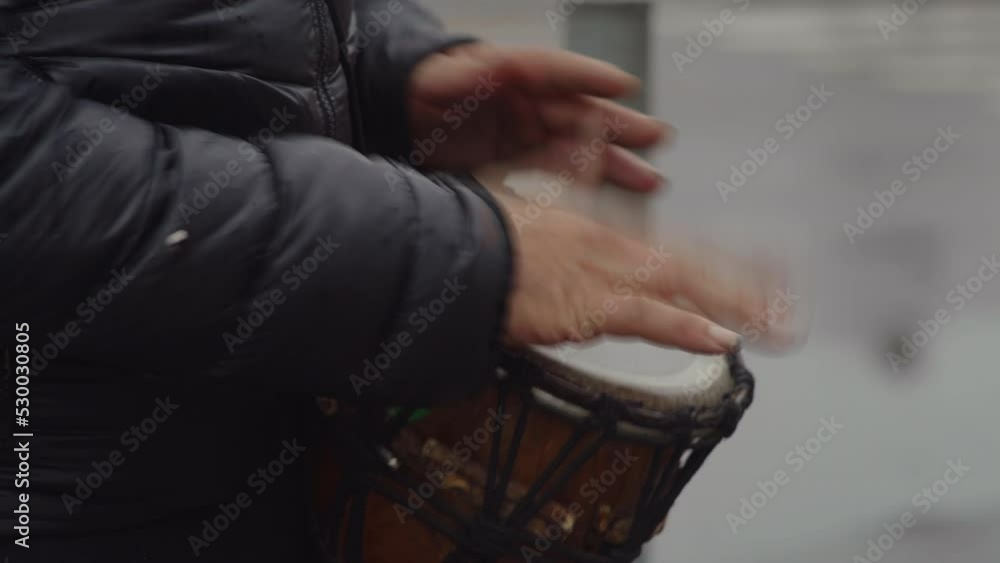 Close-up, a street musician playing an African drum after rain near a roadway Close-up, a street musician playing an African drum after rain near a roadway