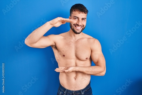 Handsome hispanic man standing shirtless gesturing with hands showing big and large size sign, measure symbol. smiling looking at the camera. measuring concept.