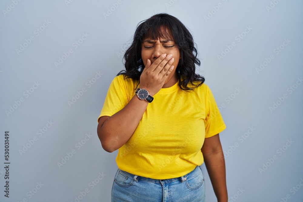Hispanic woman standing over blue background bored yawning tired covering mouth with hand. restless and sleepiness. Hispanic woman standing over blue background bored yawning tired covering mouth with hand. restless and sleepiness.