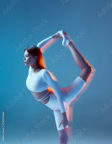 Fototapeta Naklejka Na Ścianę i Meble -  Slim flexible young girl gymnast stretching her leg up, bending lower back. Yoga, pilates workout. Long exposure