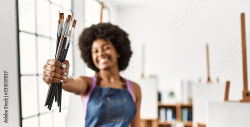 Young african american woman smiling confident holding paintbrushes at art studio
