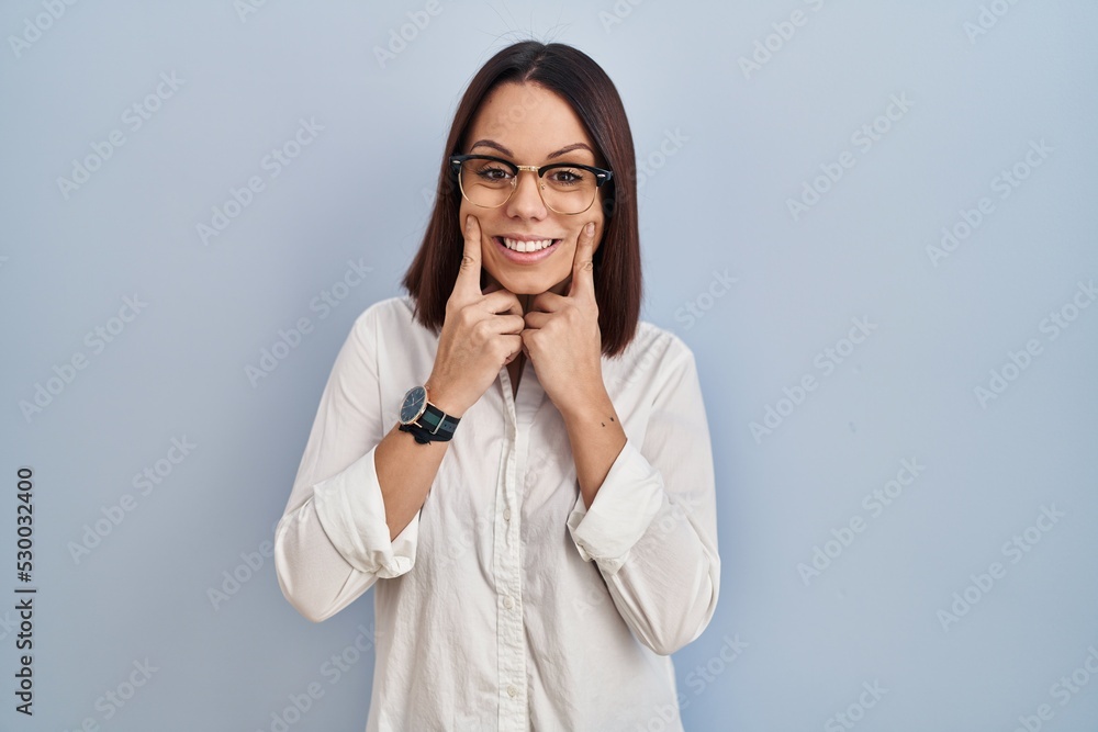 Young hispanic woman standing over white background smiling with open mouth, fingers pointing and forcing cheerful smile Young hispanic woman standing over white background smiling with open mouth, fingers pointing and forcing cheerful smile