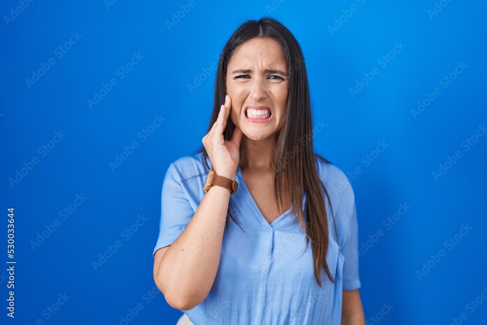 Young brunette woman standing over blue background touching mouth with hand with painful expression because of toothache or dental illness on teeth. dentist Young brunette woman standing over blue background touching mouth with hand with painful expression because of toothache or dental illness on teeth. dentist