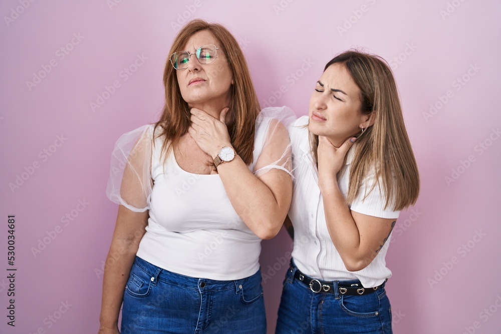 Hispanic mother and daughter wearing casual white t shirt over pink background touching painful neck, sore throat for flu, clod and infection Hispanic mother and daughter wearing casual white t shirt over pink background touching painful neck, sore throat for flu, clod and infection