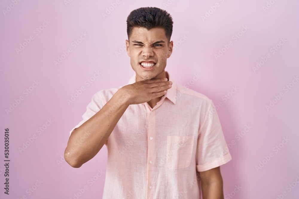 Young hispanic man standing over pink background cutting throat with hand as knife, threaten aggression with furious violence Young hispanic man standing over pink background cutting throat with hand as knife, threaten aggression with furious violence