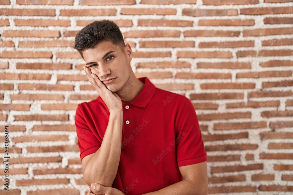 Young hispanic man standing over bricks wall thinking looking tired and bored with depression problems with crossed arms. Young hispanic man standing over bricks wall thinking looking tired and bored with depression problems with crossed arms.
