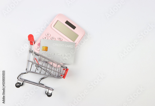  flat layout of calculator and creddit card in Shopping trolley  on white  background. Economic calculation of shopping.