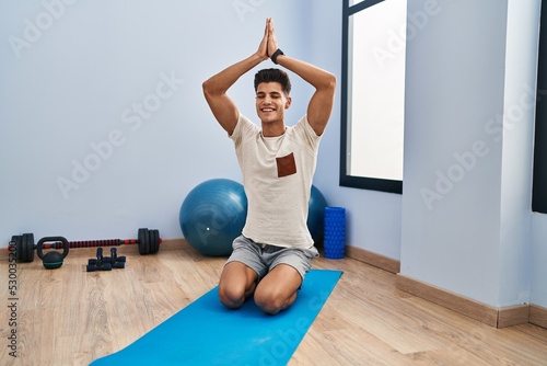 Young hispanic man smiling confident training yoga at sport center