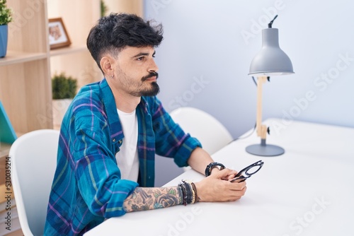 Young hispanic man sitting on table with serious expression at home photo