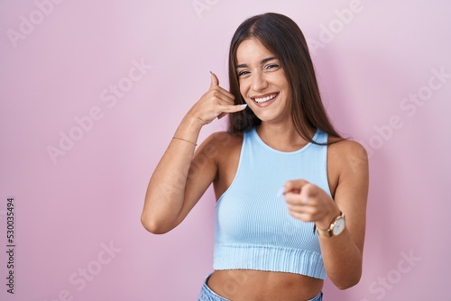 Young brunette woman standing over pink background smiling doing talking on the telephone gesture and pointing to you. call me. © Krakenimages.com