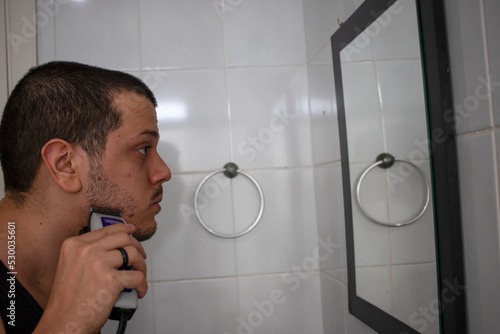 Young guy cutting his hair looking at mirror