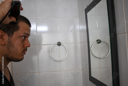 Young guy cutting his hair looking at mirror