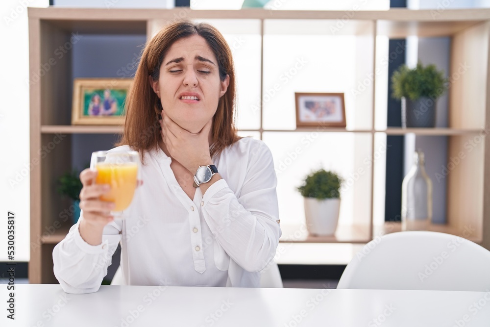Brunette woman drinking glass of orange juice touching painful neck, sore throat for flu, clod and infection Brunette woman drinking glass of orange juice touching painful neck, sore throat for flu, clod and infection