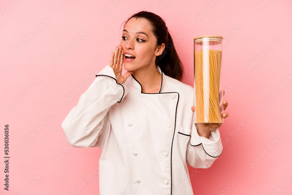 Young chef caucasian woman holding a spaghettis jar isolated on pink background shouting and holding palm near opened mouth. Young chef caucasian woman holding a spaghettis jar isolated on pink background shouting and holding palm near opened mouth.