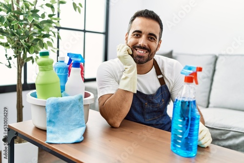 Young hispanic man smiling confident cleaning table using sprayer at home