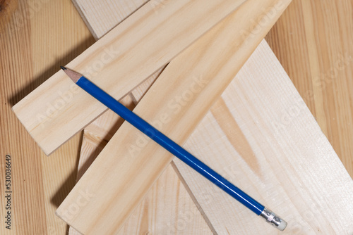 The pencil rests on wooden boards and slats for marking and sawing