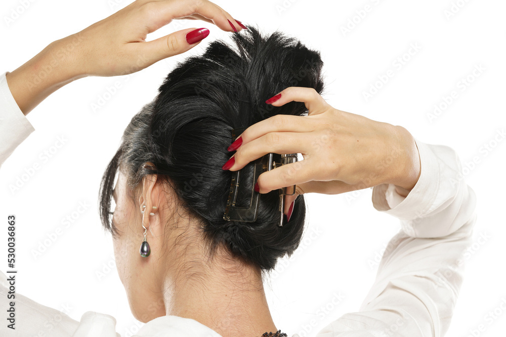 Fototapeta premium woman ties her hair with a barrette on a white background