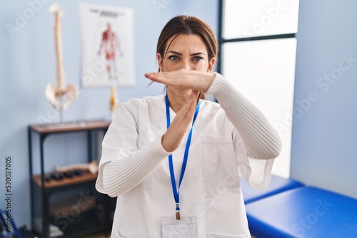 Young brunette woman working at pain recovery clinic doing time out gesture with hands, frustrated and serious face