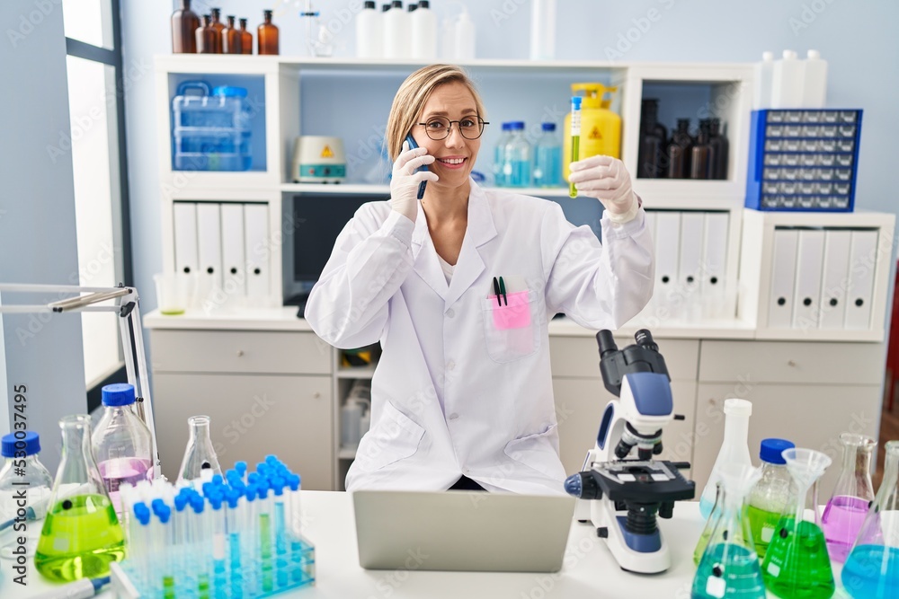 Young blonde woman scientist talking on smartphone holding test tube at laboratory Young blonde woman scientist talking on smartphone holding test tube at laboratory