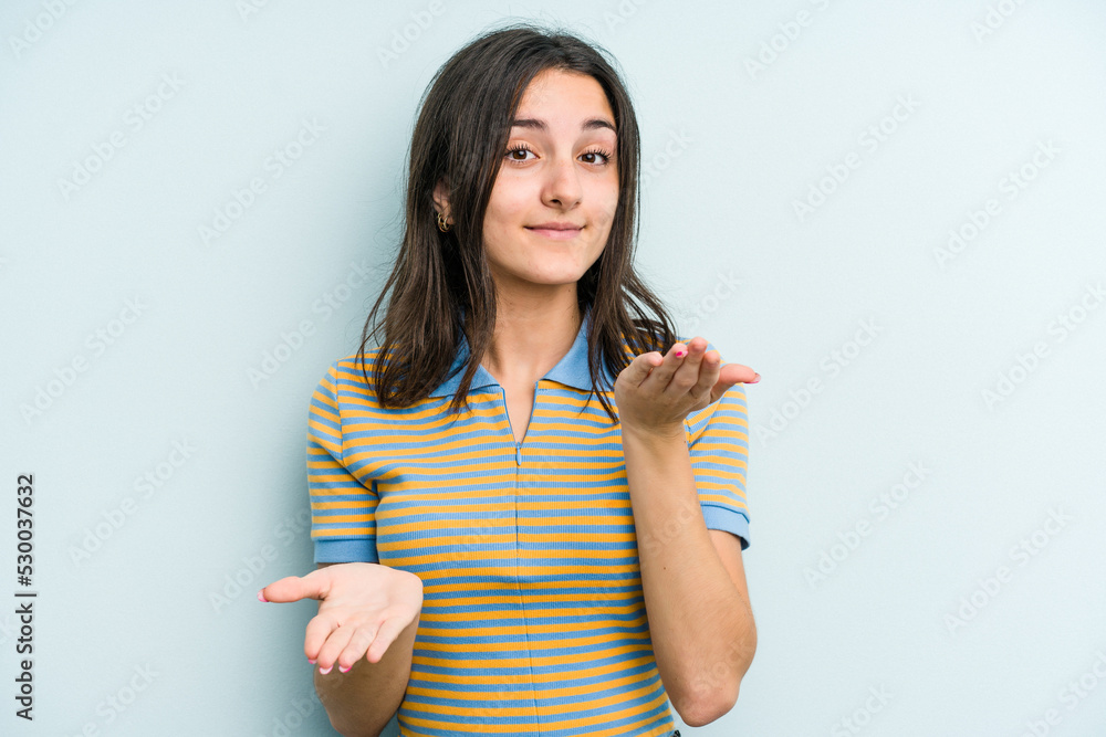 Young caucasian woman isolated on blue background makes scale with arms, feels happy and confident. Young caucasian woman isolated on blue background makes scale with arms, feels happy and confident.