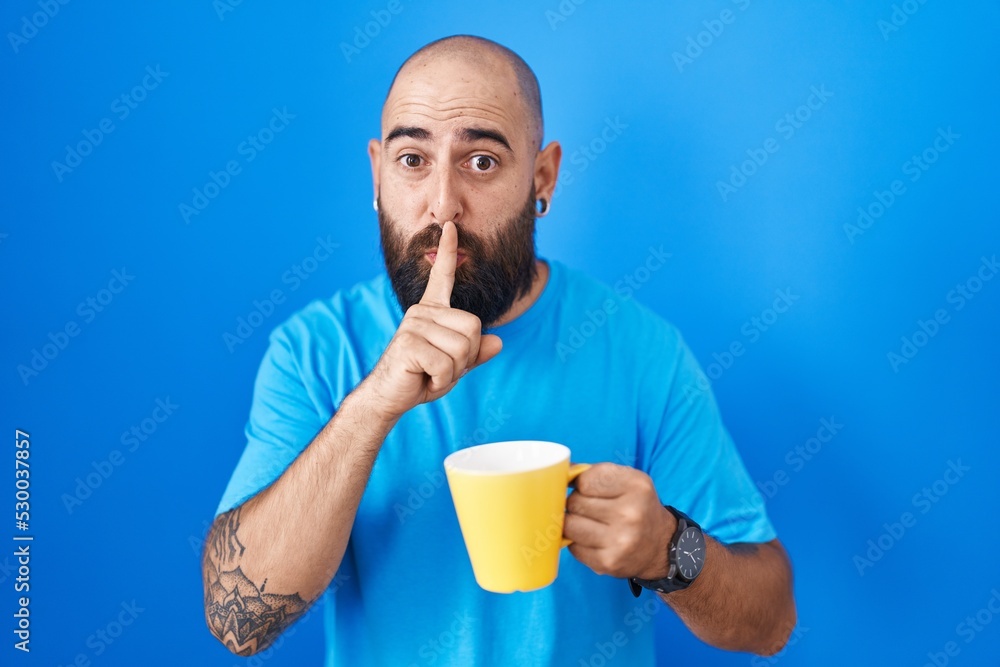 Young hispanic man with beard and tattoos drinking a cup of coffee asking to be quiet with finger on lips. silence and secret concept. Young hispanic man with beard and tattoos drinking a cup of coffee asking to be quiet with finger on lips. silence and secret concept.