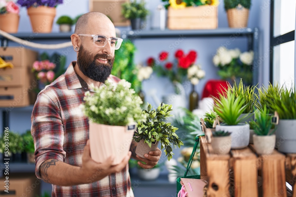 Young bald man florist holding plants at flower shop Young bald man florist holding plants at flower shop