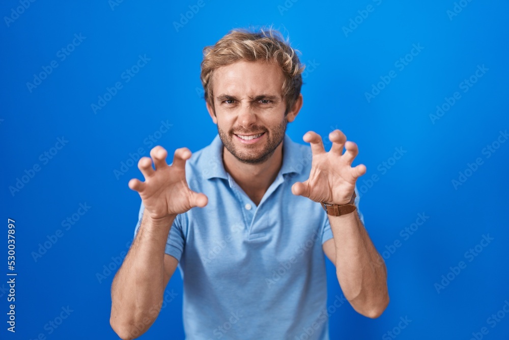 Caucasian man standing over blue background smiling funny doing claw gesture as cat, aggressive and sexy expression Caucasian man standing over blue background smiling funny doing claw gesture as cat, aggressive and sexy expression