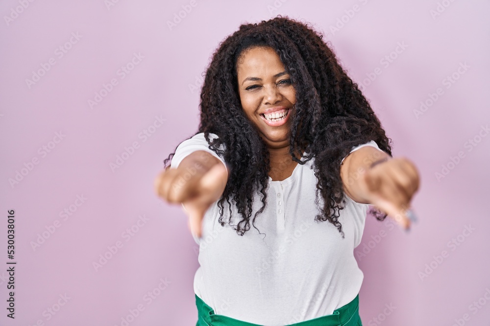 Plus size hispanic woman standing over pink background pointing to you and the camera with fingers, smiling positive and cheerful Plus size hispanic woman standing over pink background pointing to you and the camera with fingers, smiling positive and cheerful