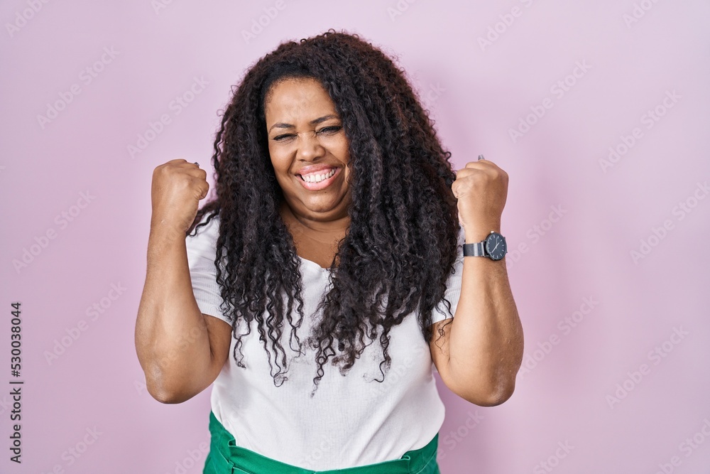 Plus size hispanic woman standing over pink background celebrating surprised and amazed for success with arms raised and eyes closed. winner concept. Plus size hispanic woman standing over pink background celebrating surprised and amazed for success with arms raised and eyes closed. winner concept.