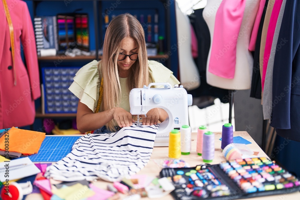 Fototapeta premium Young beautiful hispanic woman tailor using sewing machine at clothing factory