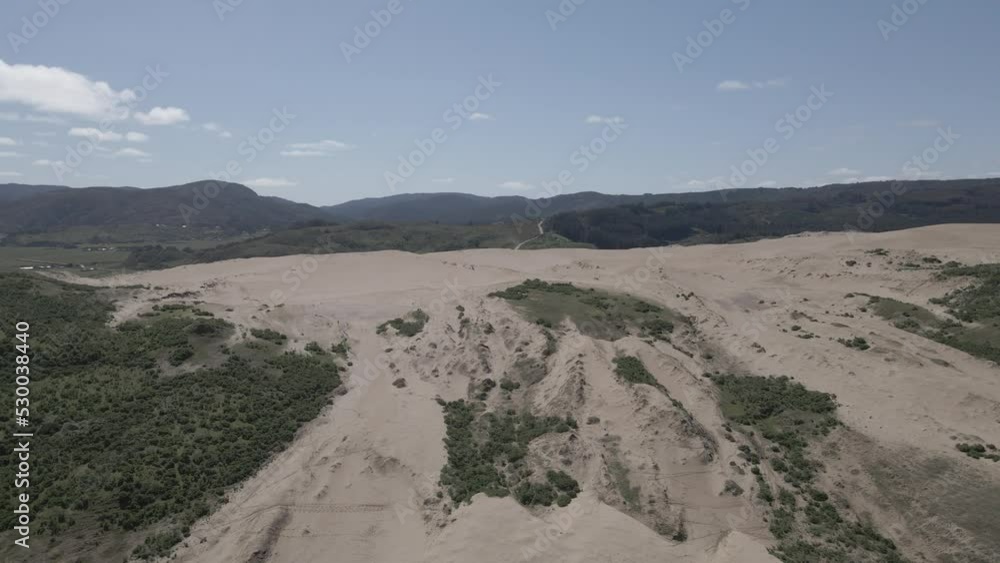 Push in aerial shot of sand dunes in Llani, Chile with bushes on the sides and mountains in the background taken during a clear sunny day with some clouds. Push in aerial shot of sand dunes in Llani, Chile with bushes on the sides and mountains in the background taken during a clear sunny day with some clouds.