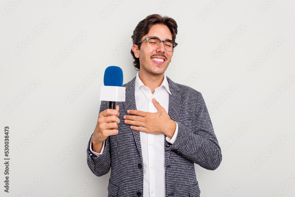 Young hispanic TV presenter man isolated on white background laughs out loudly keeping hand on chest. Young hispanic TV presenter man isolated on white background laughs out loudly keeping hand on chest.