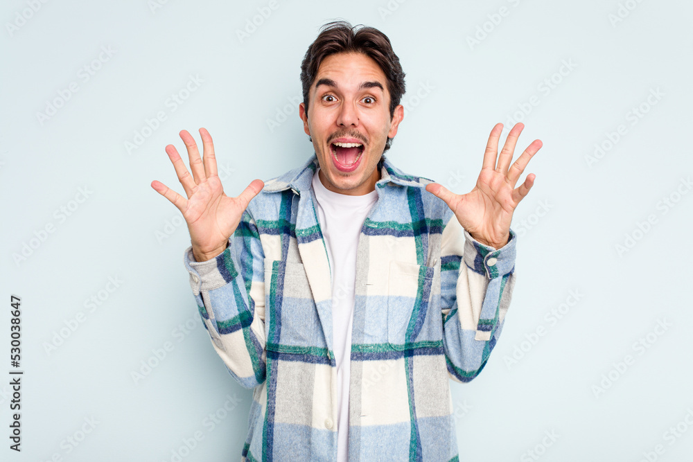 Naklejka premium Young hispanic man isolated on blue background celebrating a victory or success, he is surprised and shocked.