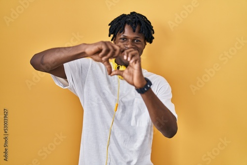 Young african man with dreadlocks standing over yellow background smiling in love doing heart symbol shape with hands. romantic concept.