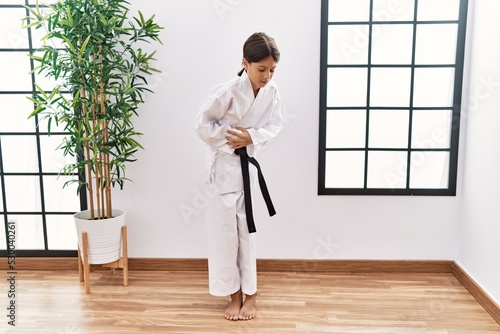 Young hispanic girl wearing karate kimono and black belt with hand on stomach because nausea, painful disease feeling unwell. ache concept.