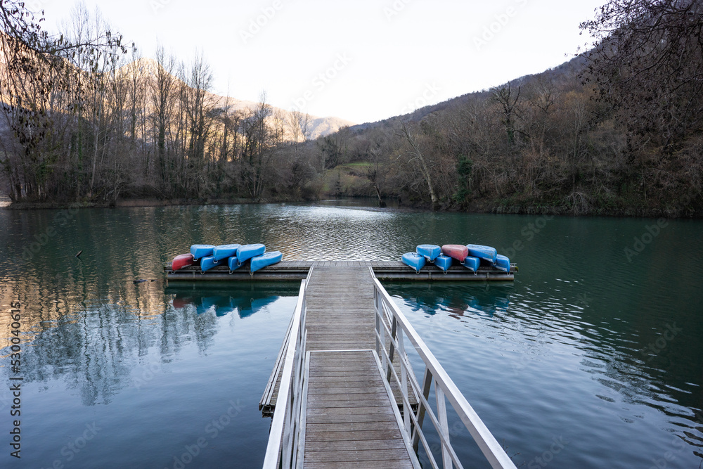 Embalse con pasarela de madera y canoas apiladas sobre ella en una tarde de otoño