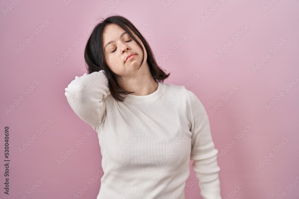 Woman with down syndrome standing over pink background suffering of neck ache injury, touching neck with hand, muscular pain Woman with down syndrome standing over pink background suffering of neck ache injury, touching neck with hand, muscular pain