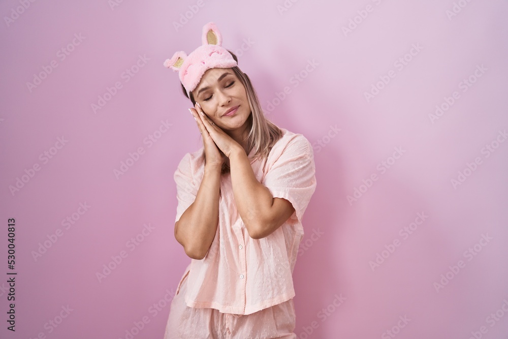 Blonde caucasian woman wearing sleep mask and pajama sleeping tired dreaming and posing with hands together while smiling with closed eyes. Blonde caucasian woman wearing sleep mask and pajama sleeping tired dreaming and posing with hands together while smiling with closed eyes.