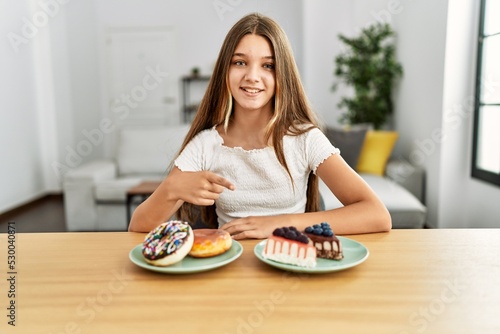 Young brunette teenager eating cakes and sweets smiling happy pointing with hand and finger