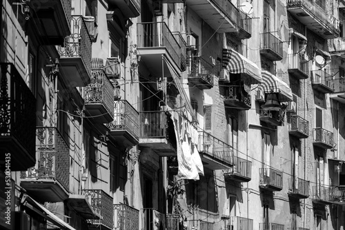 Facade in a narrow street in old town “Centro storico“ of historic italian metropole Naples. Balconys of typical residential building block of flats in rotten and weathered condition, black and white. photo