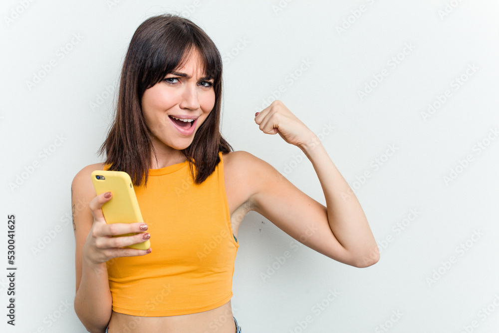 Young caucasian woman using mobile phone isolated on white background raising fist after a victory, winner concept. Young caucasian woman using mobile phone isolated on white background raising fist after a victory, winner concept.