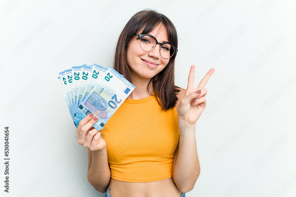Young caucasian woman holding a banknotes isolated on blue background showing number two with fingers. Young caucasian woman holding a banknotes isolated on blue background showing number two with fingers.