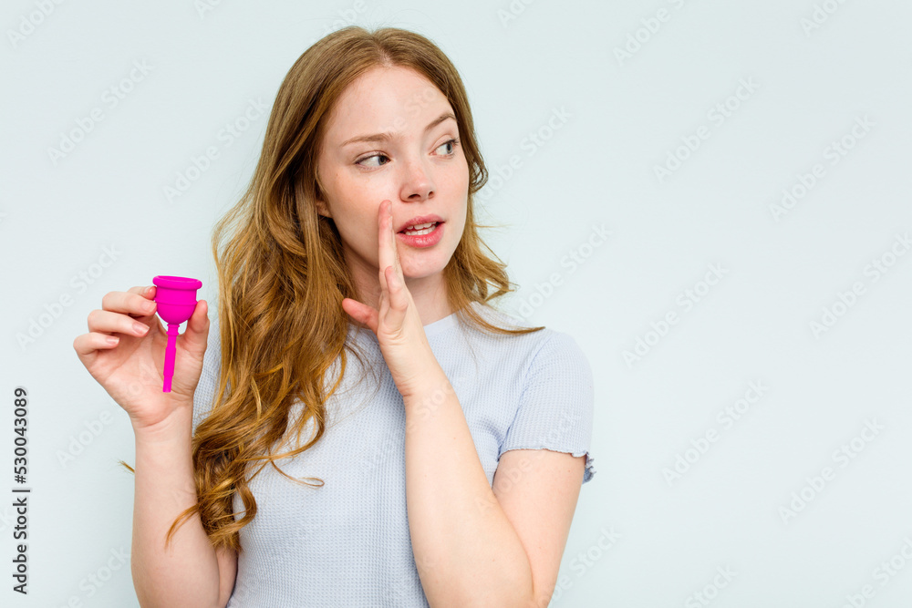 Young caucasian woman holding menstrual cup isolated on blue background is saying a secret hot braking news and looking aside Young caucasian woman holding menstrual cup isolated on blue background is saying a secret hot braking news and looking aside